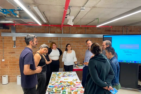 Grup de persones participant en una dinàmica de cocreació al voltant d’una taula amb materials visuals.