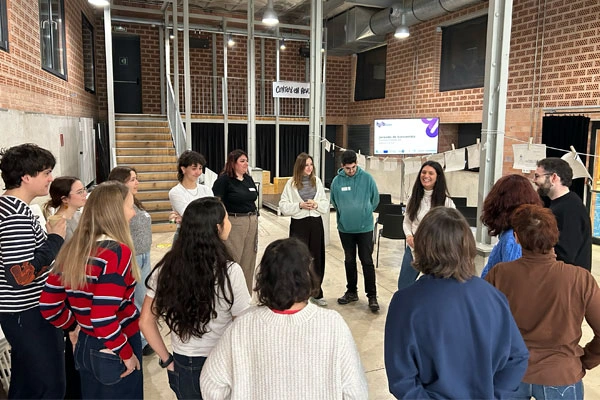 Grup de persones participant en una dinàmica en rotllana en un espai comunitari, amb una facilitadora conduint la sessió.