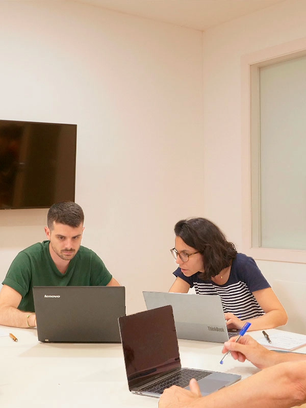 Persones treballant en una reunió amb ordinadors portàtils i documents.