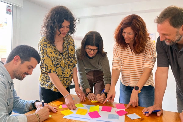 Grup de persones participant en un taller col·laboratiu, treballant amb notes adhesives de colors sobre una taula.