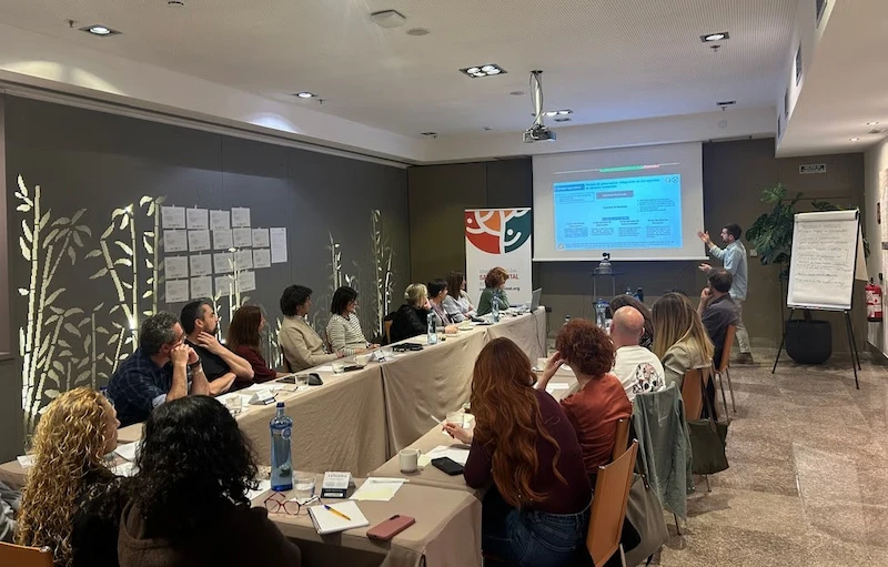 Persones treballant en grups al voltant de diverses taules durant una sessió participativa en un espai de formació.